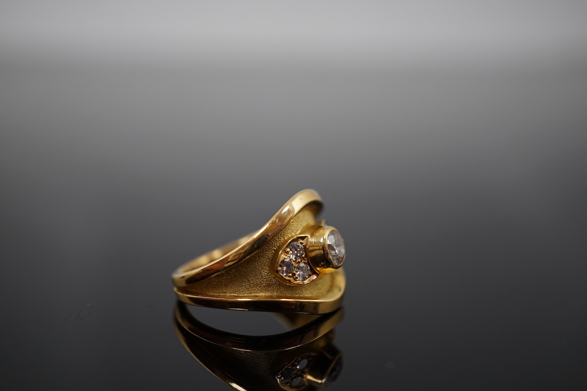 A 1990's part textured 18ct gold and collet set single stone diamond ring by Leo De Vroomen, with six stone diamond set shoulders, retailed by Boodle & Dunthorne